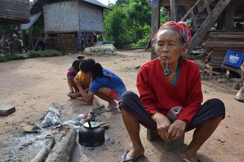 an older woman sitting next to a fire with two children at Tulip Hotel in Louang Namtha
