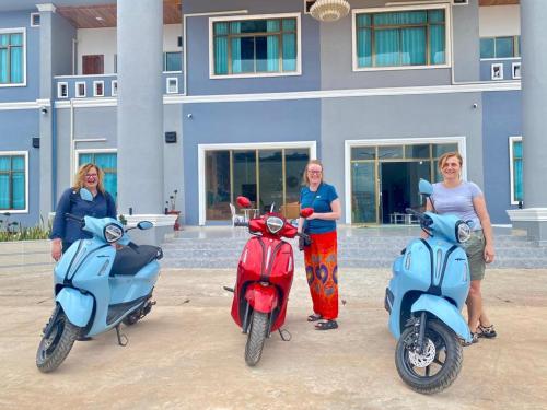 three women standing next to their scooters in front of a building at Tulip Hotel in Louang Namtha