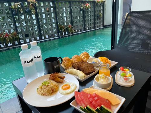 a table topped with plates of food next to a pool at NANEE Phra Singh - Adults Only in Chiang Mai