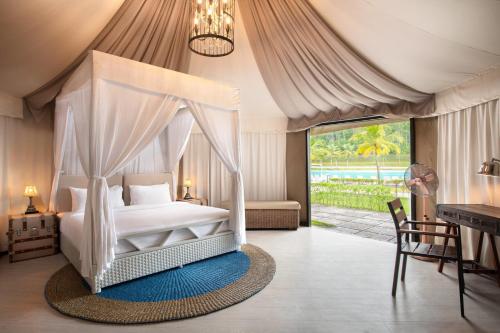 a bedroom with a canopy bed with a table and a desk at Natra Bintan, a Tribute Portfolio Resort in Lagoi
