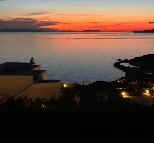 una puesta de sol sobre un cuerpo de agua con un edificio en White Rock Suites & Villas, en Houlakia