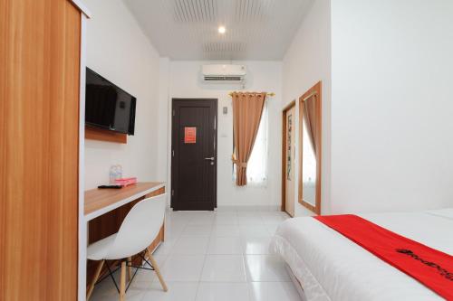 Schlafzimmer mit einem Bett, einem Schreibtisch und einem TV in der Unterkunft RedDoorz Plus Syariah near Mall Boemi Kedaton Lampung in Kedaton