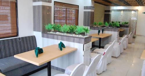 un restaurante con mesas, sillas blancas y plantas en HOTEL PARTH EXECUTIVE, en Lātūr