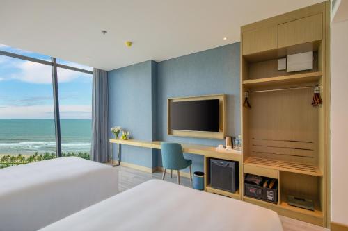 a bedroom with a bed and a desk with a television at Awaken Da Nang Hotel in Da Nang