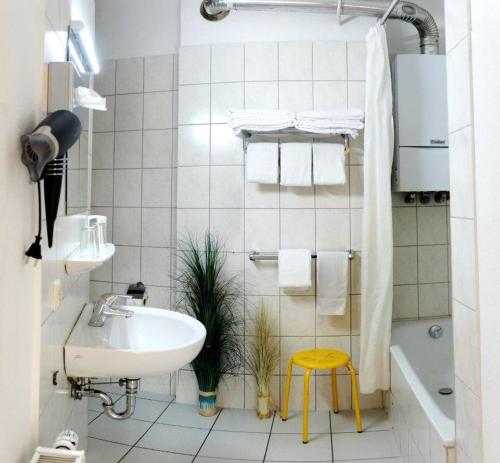 a white bathroom with a sink and a yellow stool at Hotel Lousberg in Aachen