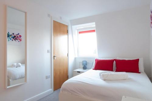 a bedroom with a white bed with red pillows and a mirror at *New* 2-Bed Modern Apartment in Burton upon Trent