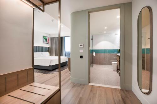 a bathroom with a large mirror and a bedroom at Holiday Inn & Suites Geelong by IHG in Geelong