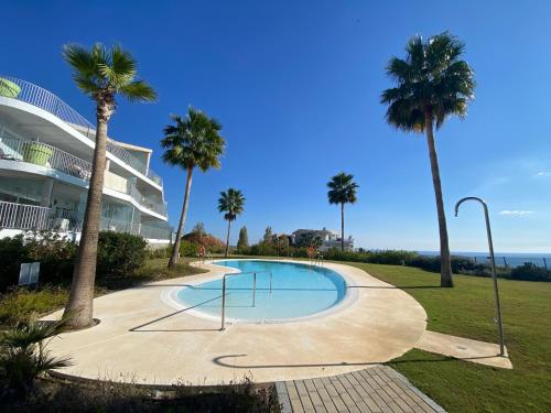 a swimming pool with palm trees in front of a building at Relax in Reserva del Higuerón - Crystalline in Benalmádena