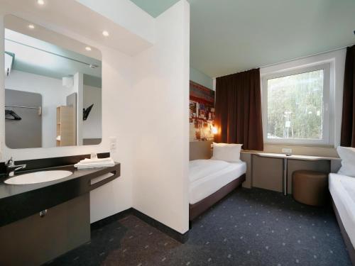 een badkamer met een bed, een wastafel en een spiegel bij B&B Hotel Berlin-Dreilinden in Kleinmachnow