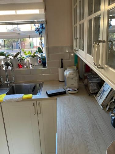 cocina con armarios blancos, fregadero y ventana en Angels Pad, en Dagenham