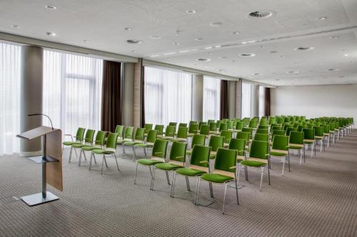 een vergaderzaal met groene stoelen en een podium bij IntercityHotel Breda in Breda