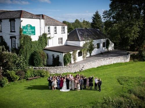 a group of people standing in the grass in front of a building at The Ken Bridge Hotel in New Galloway