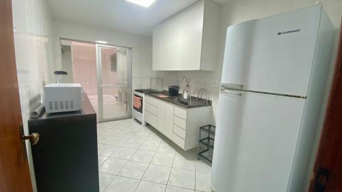 La cuisine blanche est équipée d'un réfrigérateur et d'un évier. dans l'établissement Apartamento encantador a uma quadra do melhor trecho da Praia do forte- Cabo Frio, à Cabo Frio
