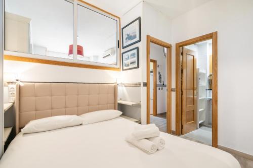a bedroom with a bed with white sheets and a mirror at Geranios 32 (Plaza Castilla) in Madrid