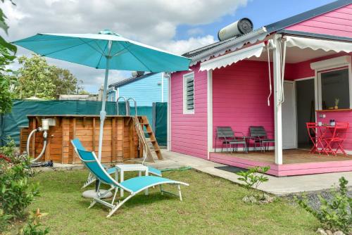 uma casa cor-de-rosa com uma cadeira e um guarda-chuva em Les jardins de CHANTILLY -Bungalows 4 étoiles avec jardins et piscines privées em Baie-Mahault