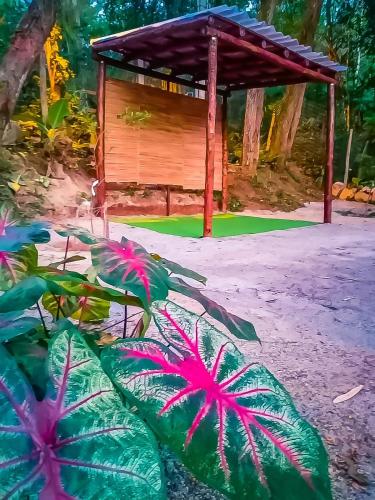a wooden shelter with pink flowers in front of a plant at Chalé 03 Itaipu Vale da Colina Niterói in Niterói