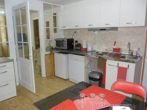 cocina con armarios blancos, fregadero y mesa en Meublé Bulgarana - 4 pers en Bourg-Argental