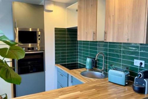 - une cuisine avec évier et carrelage vert sur le mur dans l'établissement Le tropical - T2 42m2 - centre ville - parking, à Montauban