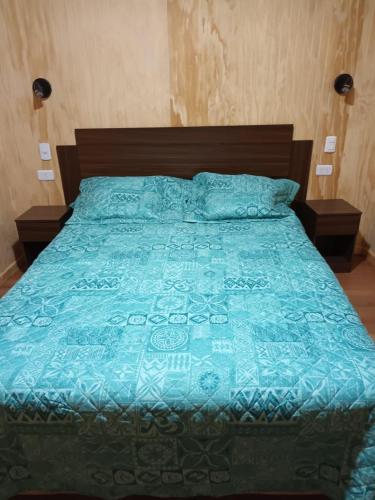 a bed with a blue comforter and pillows at Cabaña Los Raulies, Neltume in Puerto Fuy