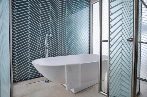 uma banheira na casa de banho com uma parede de vidro em Aerotel Muscat - Airport Transit Hotel em Mascate