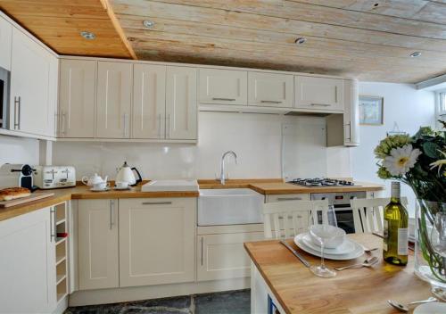 パドストウにあるSunbeam Cottageの白いキャビネットと木製の天井が備わるキッチン