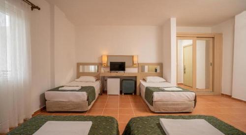 a room with three beds and a desk with a television at MALİBU RESORT in Kemer