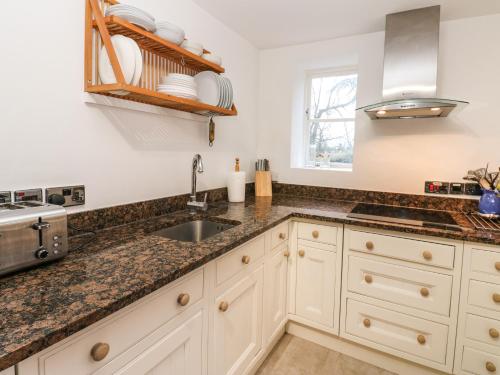 una cocina con armarios blancos y fregadero en Malt Shovel Cottage en Bedale