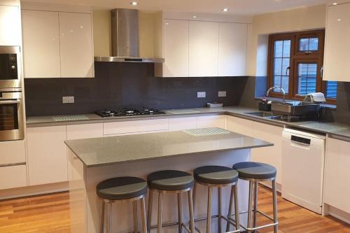 a kitchen with a island with four stools at Luxury London House Sleeps x 16, Free Parking, Free Wifi, Garden Patio, Close to tube line easy access to Central London in Ilford