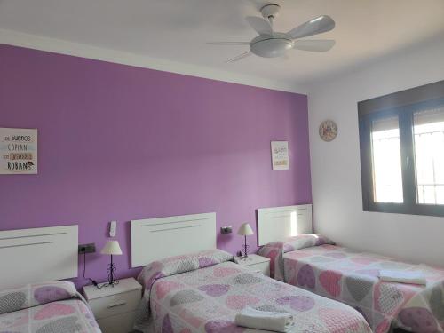 a room with three beds and a purple wall at Relax, vistas, barbacoa y piscina, junto a Ronda in Arriate