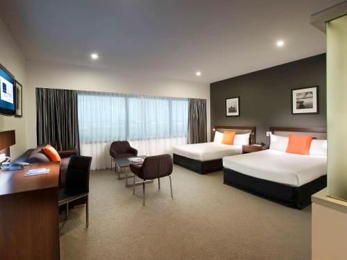 a hotel room with two beds and a desk at Novotel Brisbane Airport in Brisbane