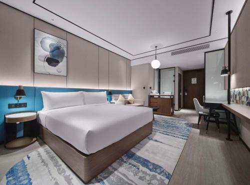 南通市にあるHilton Garden Inn Nantong Rudongの大きなベッドとデスクが備わるホテルルームです。