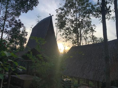 a building with a roof with the sun in the background at Khu Du Lịch Sinh Thái, Nghỉ dưỡng Homestay Hoàng Ánh - Kon Xom Luh in Kon Tum