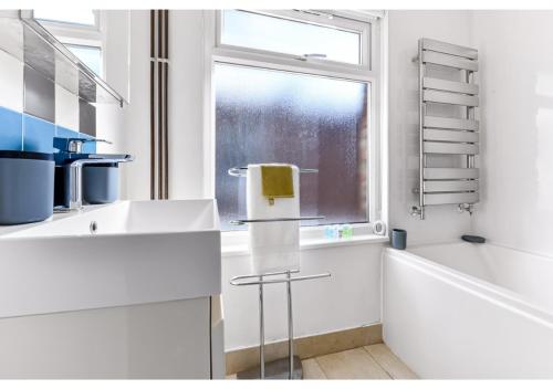 ein weißes Badezimmer mit einem Fenster, einer Badewanne und einem Waschbecken in der Unterkunft Earth Tones & Greenery: 4BR Flat Sleeps 8 in London