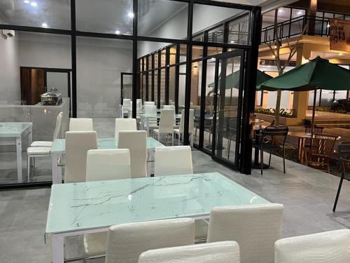 un comedor con sillas blancas, mesas y ventanas en Genio Syariah Hotel Solo en Colomadu