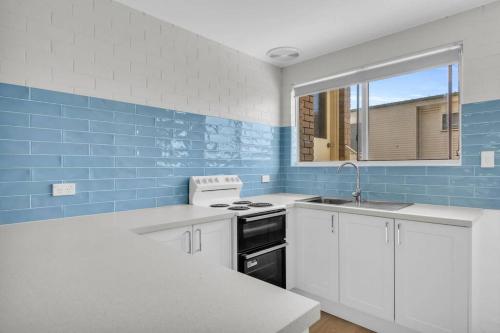 a kitchen with white cabinets and blue tiles at Marine Court - Unit 6 in Merimbula