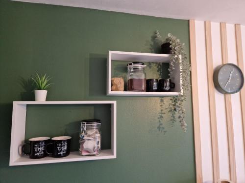 a shelf with jars and a clock on a green wall at Bel appartement rénové (Le Nichoir) in Cornimont