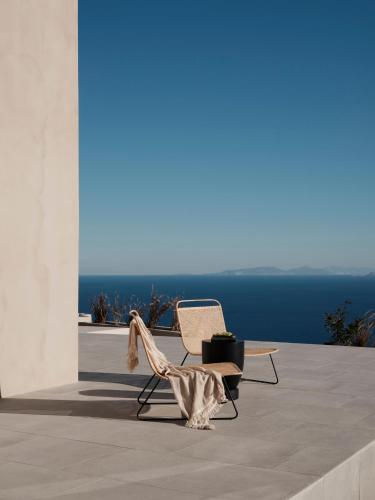 two chairs sitting on a patio with the ocean in the background at Ethos Retreat Imerovigli, Santorini in Imerovigli
