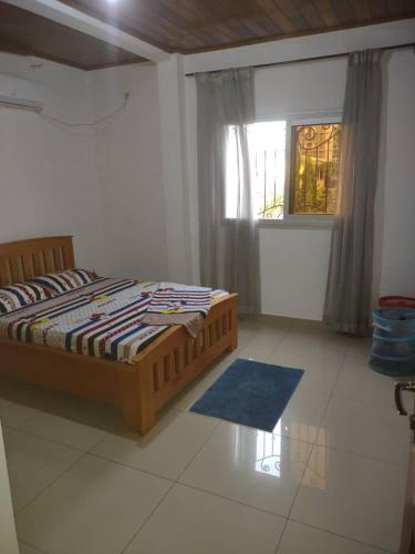 a bedroom with a bed with a blue rug and a window at Appartement charmant logpom in Douala