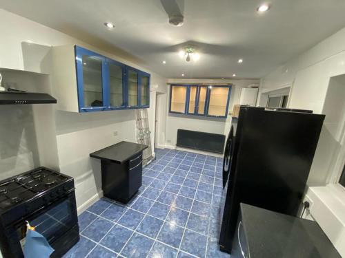 eine Küche mit einem schwarzen Kühlschrank und einem blauen Fliesenboden in der Unterkunft 4 Bed House Near Heathrow Airport with easy access into Central London in Hounslow