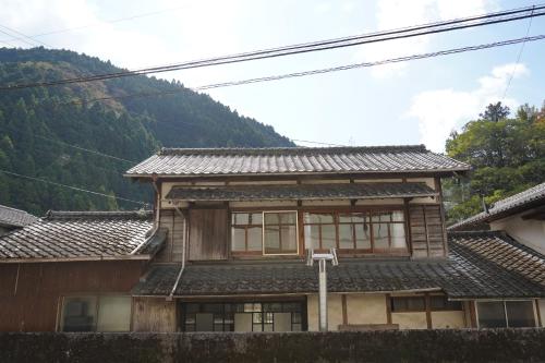a wooden house with mountains in the background at TOSAYAMA BASE 清流沿いの里山　古民家貸切　高知市街地より車で約20分 in Kochi