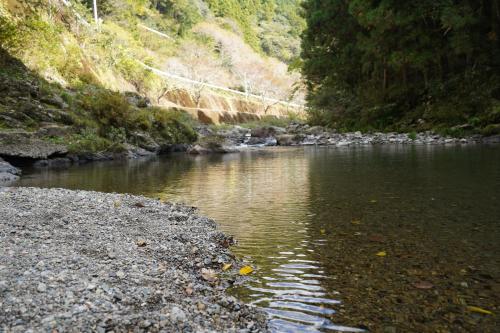 a river with a rocky shore with trees and rocks at TOSAYAMA BASE 清流沿いの里山　古民家貸切　高知市街地より車で約20分 in Kochi
