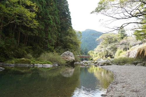 a river with trees and a bridge in the background at TOSAYAMA BASE 清流沿いの里山　古民家貸切　高知市街地より車で約20分 in Kochi