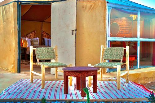 two chairs and a table on a rug in front of a house at Sky View Camp in Merzouga