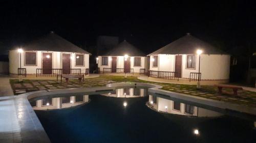 a swimming pool in front of some huts at night at The Village Resort in Kodāe