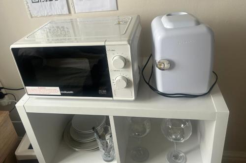 a white microwave on a shelf with wine glasses at We have a choice of 1 of 3 separate rooms in our home, a double room upstairs, a large double with en suite downstairs or a bar b q lodge in the garden with its own toilet and shower facilities please book the room you would like to stay in in Portishead