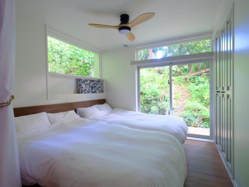a bedroom with a white bed with a ceiling fan at Yama'oto - Nature Luxury Stay in Motobu