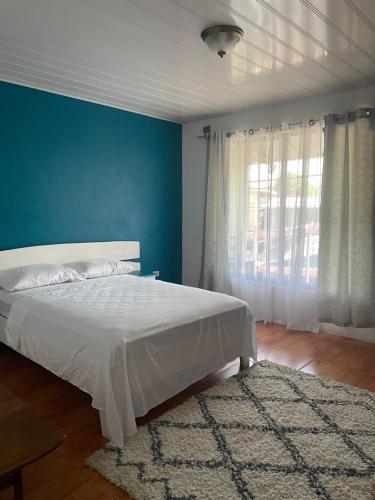 a bedroom with a white bed and a blue wall at Cómodo dormitorio in Quepos