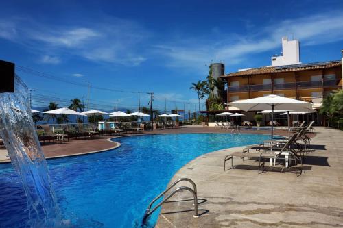 a swimming pool with a fountain and tables and umbrellas at Hotel Costa Norte Massaguaçu in Caraguatatuba