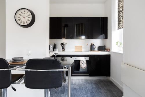 City-Centric Living Cozy 1-Bedroom Apartment في برادفورد: مطبخ مع دواليب سوداء وساعة على الحائط