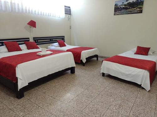 Zimmer mit 3 Betten mit roter und weißer Bettwäsche in der Unterkunft Hotel Resident Piura in Piura